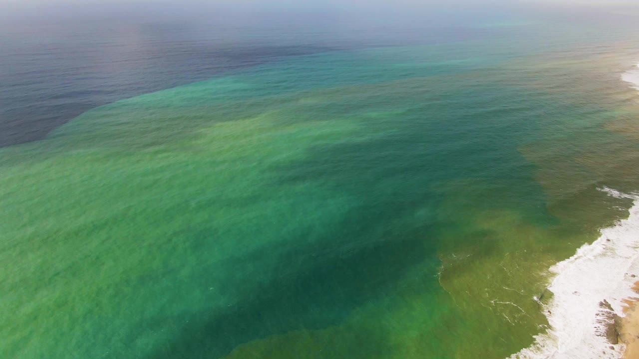 Aerial frame over Punta Gorda, Baja California Sur, showing layered turquoise and green ocean water meeting a pale surf line at the right edge, with no visible people.