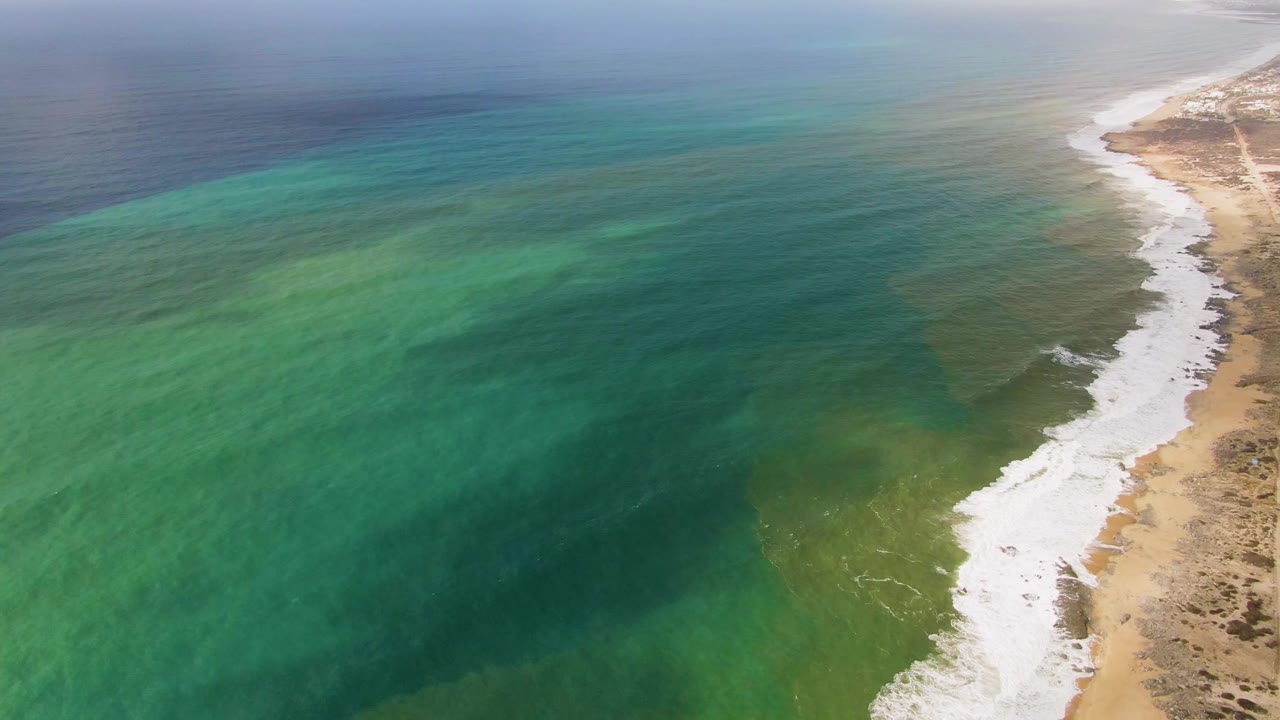 Wide aerial view of green ocean water and a curving sandy beach