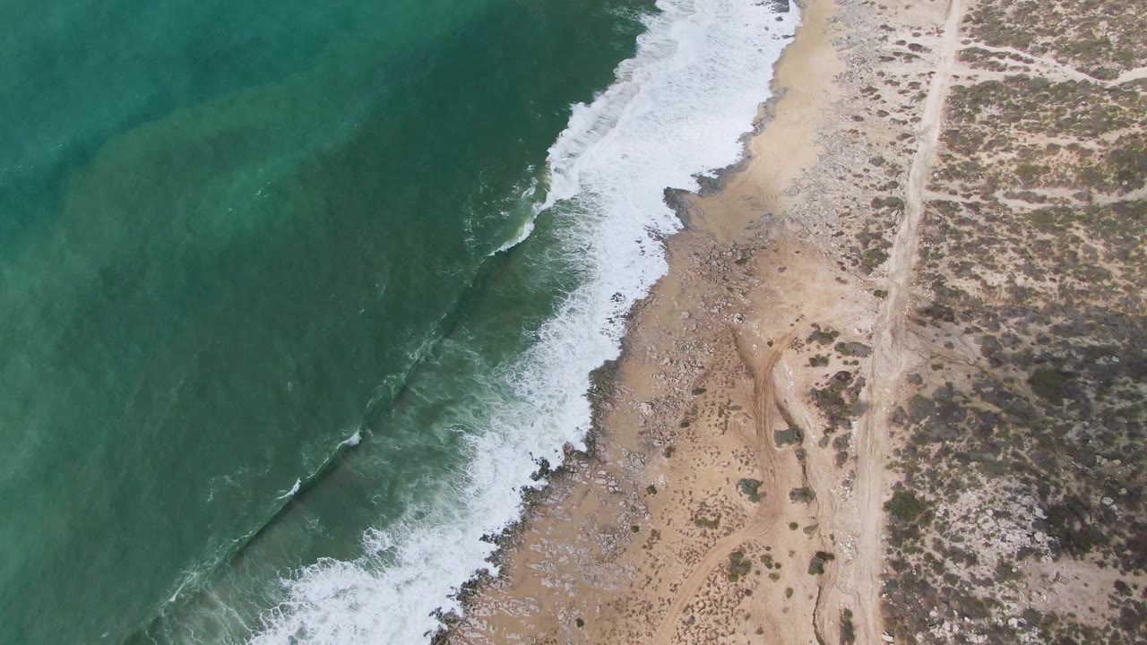 Aerial view of green surf breaking along a sandy and rocky beach
