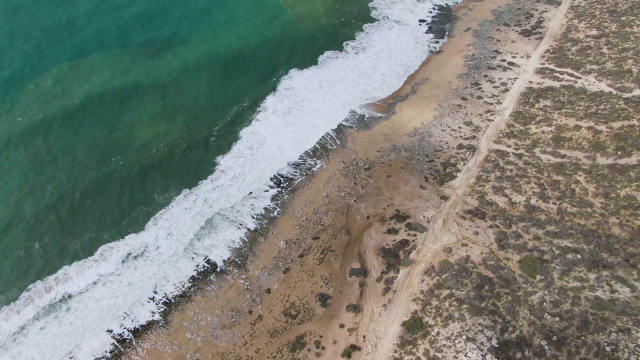 Overhead wave foam reaching farther across a sandy beach