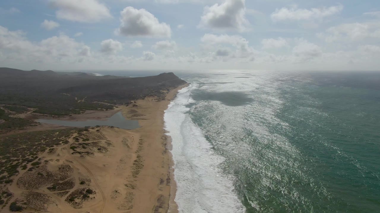 Aerial view of sandy beach, lagoon, surf, ocean, and low hills