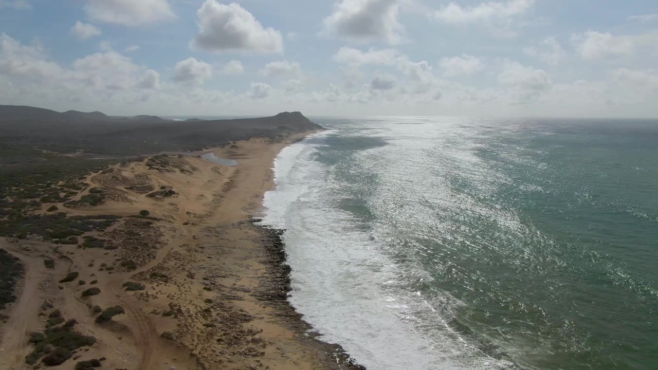 Aerial view of waves breaking along a sandy dune-backed shoreline.