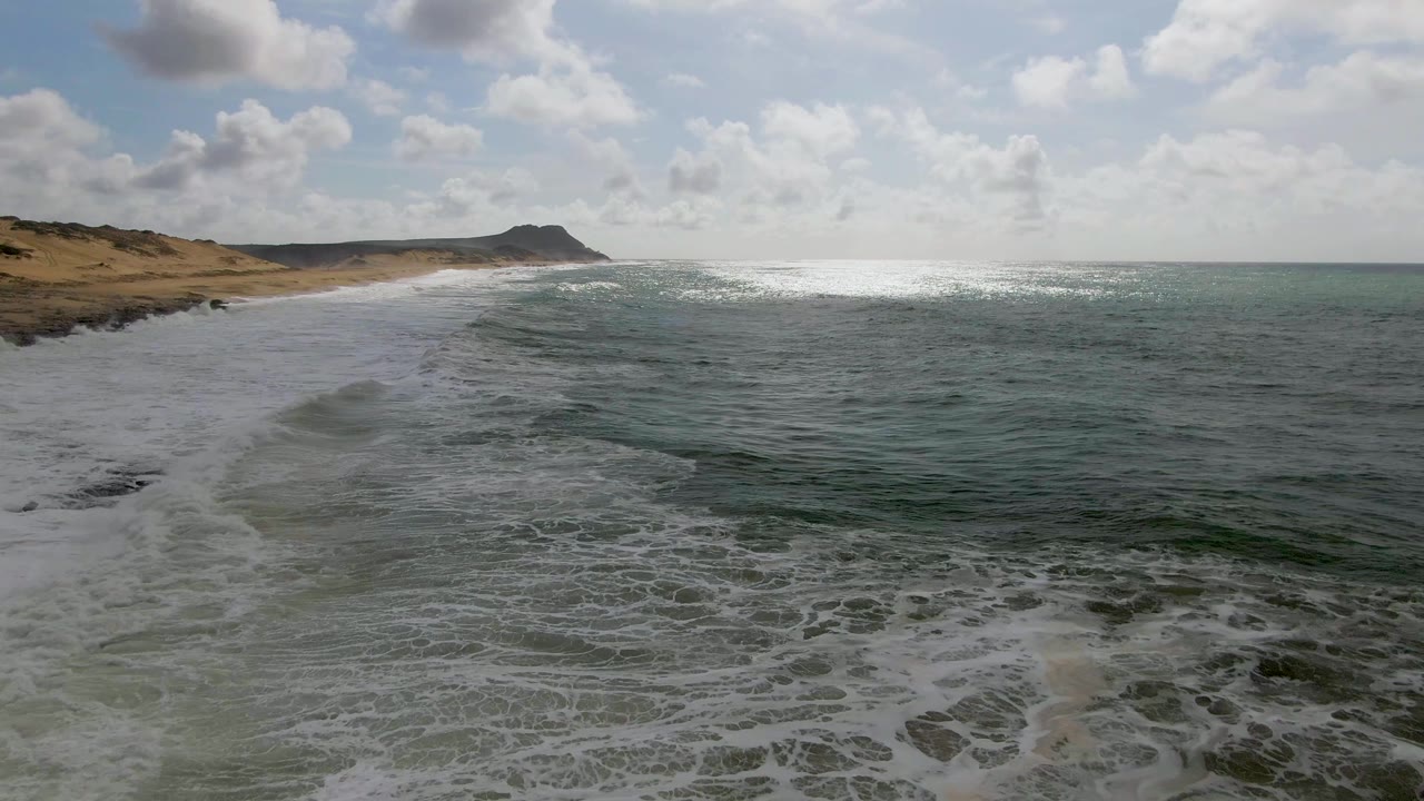 Diagonal beach and receding white foam beneath a bright cloudy sky