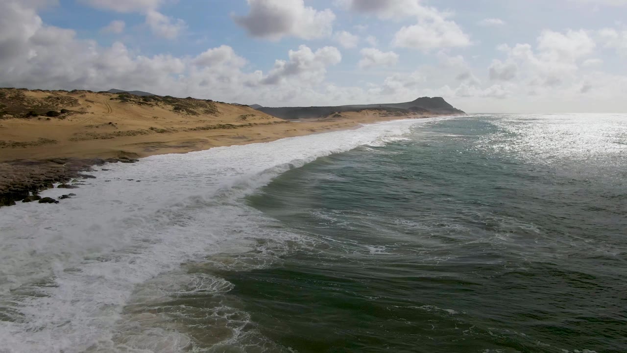 At Punta Gorda on the East Cape of Baja California Sur, foamy surf blankets the left beach edge while darker green water sits in the foreground and no people are visible.