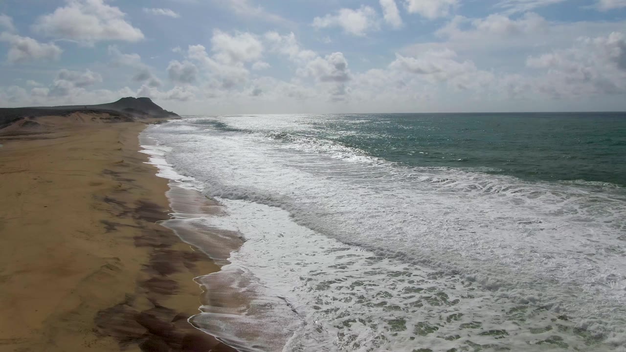 At 0:02, the Punta Gorda shoreline runs diagonally through the frame as white breakers cover much of the near shore, with open sea to the right and no visible people.