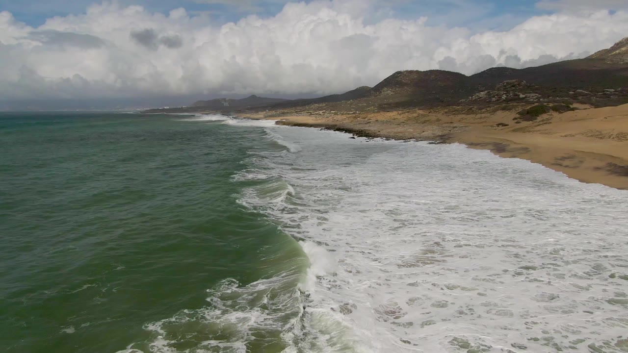 Wide aerial coastline with waves breaking near a sandy beach.