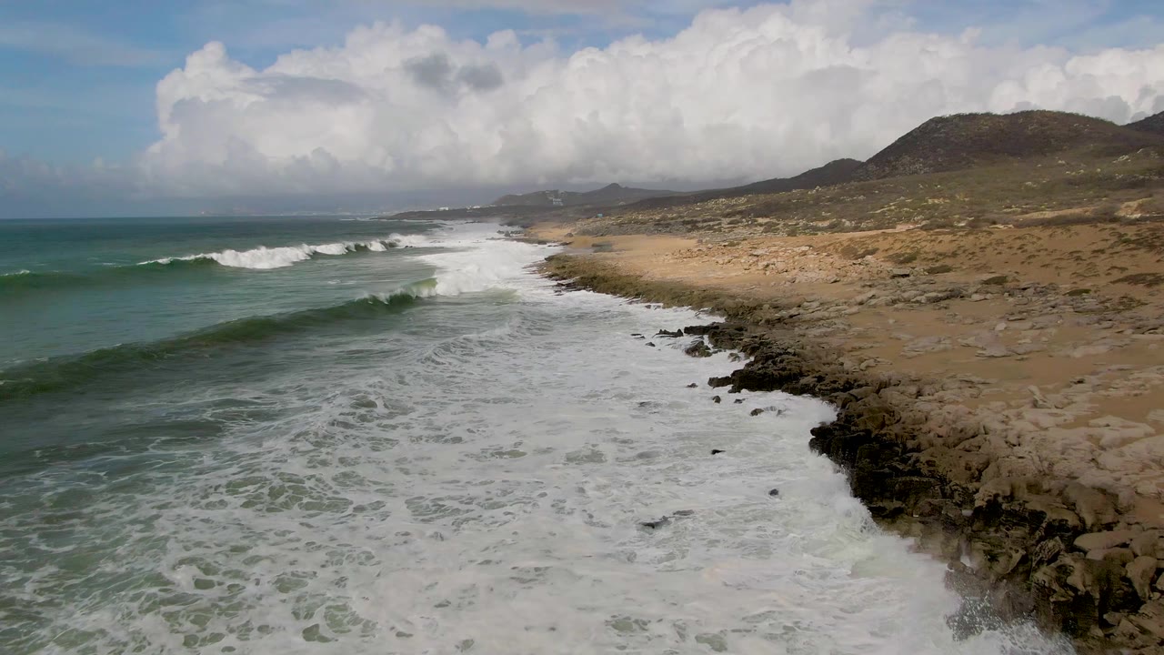 Surf washes along a rocky point beside a sandy coastal stretch.