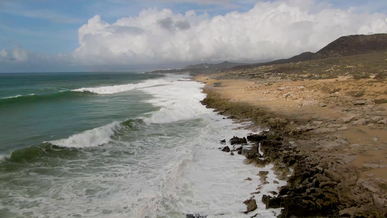 Aerial coast with waves breaking beside sandy beach and rocky outcrops