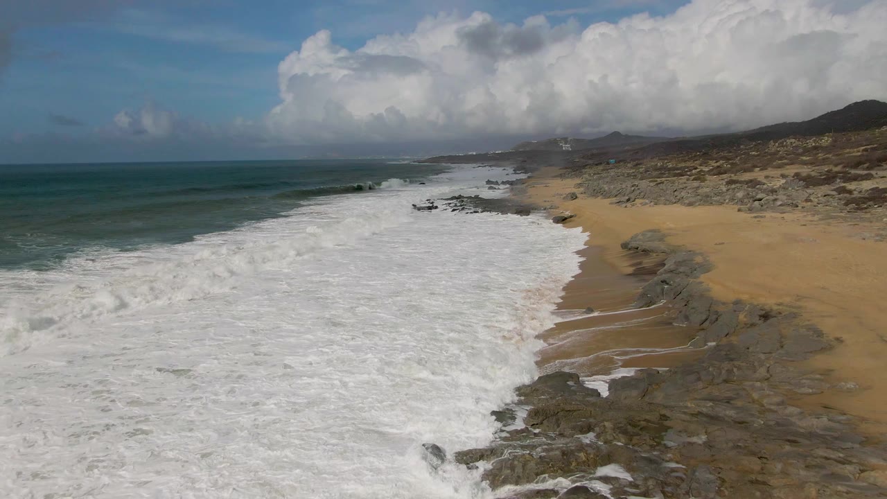 Whitewater spreads along a sandy shoreline beside rocks.