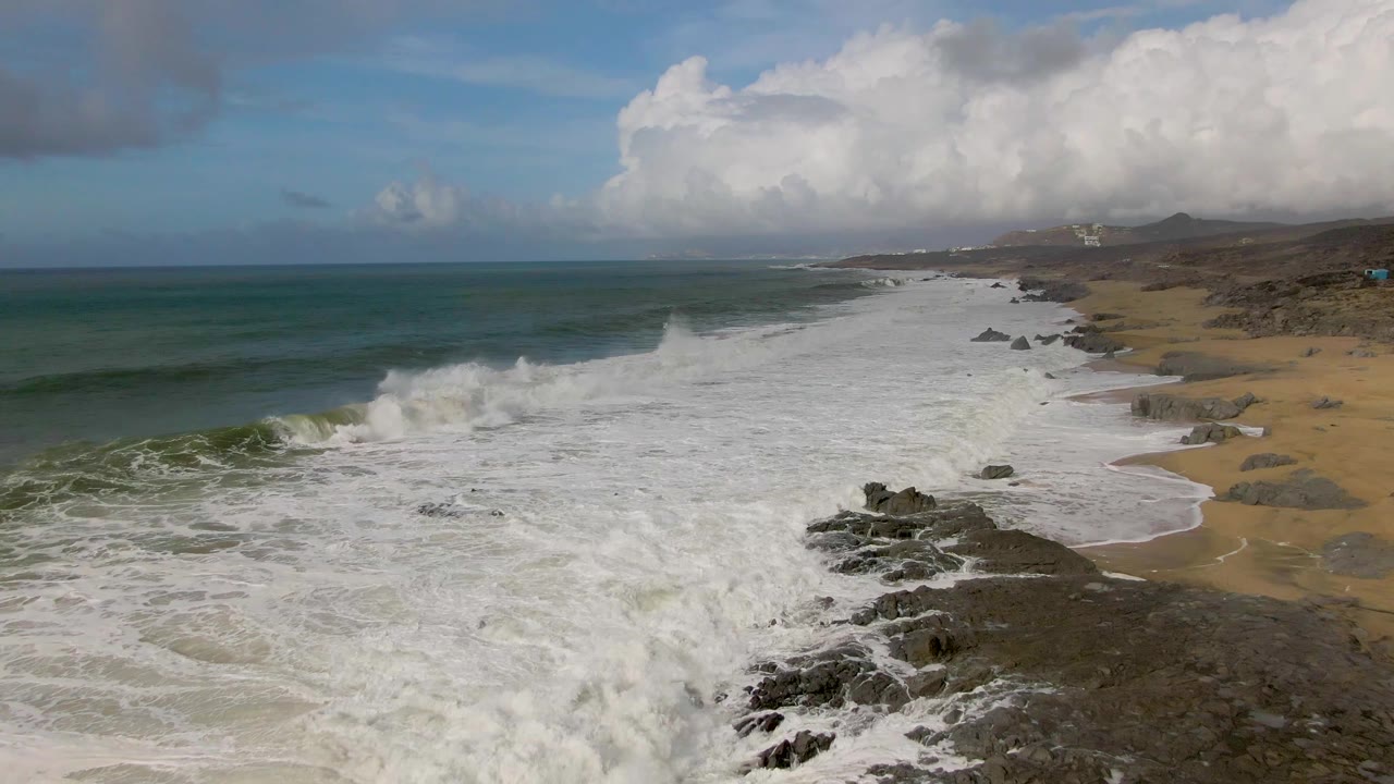 Whitewater surges across the rocky and sandy shore at Punta Gorda, with the coastline stretching into the distance and no visible people.