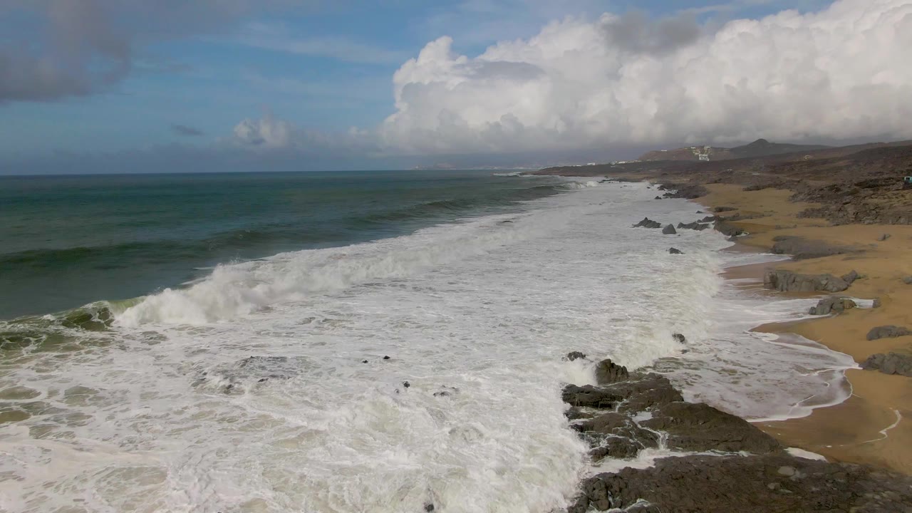Wide aerial coastline with surf washing across beach and rocks