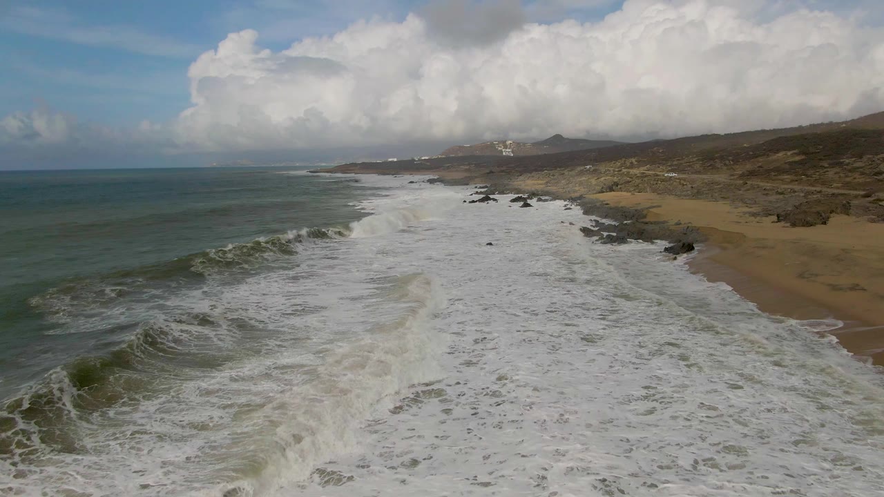 Large white surf field runs along a beach with ocean to the left and rocks to the right.