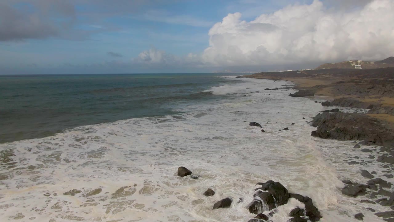 Aerial coastal view with a large rock in the foamy foreground.