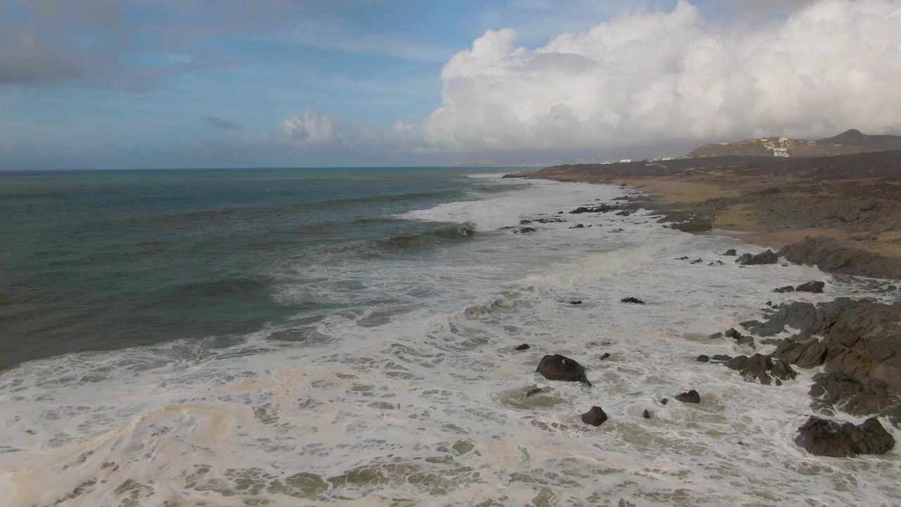 Aerial view of waves breaking over a rocky shoreline with clouds above.