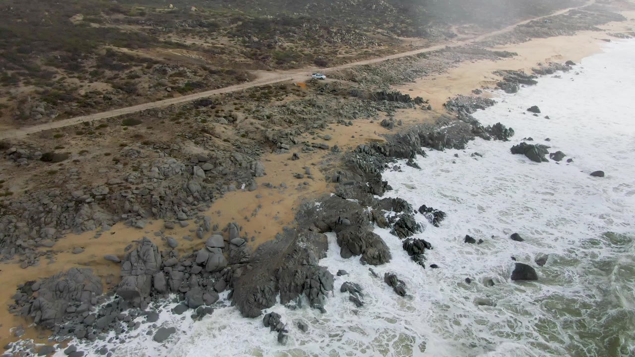 Aerial coastal landscape with a car on the road and surf below.