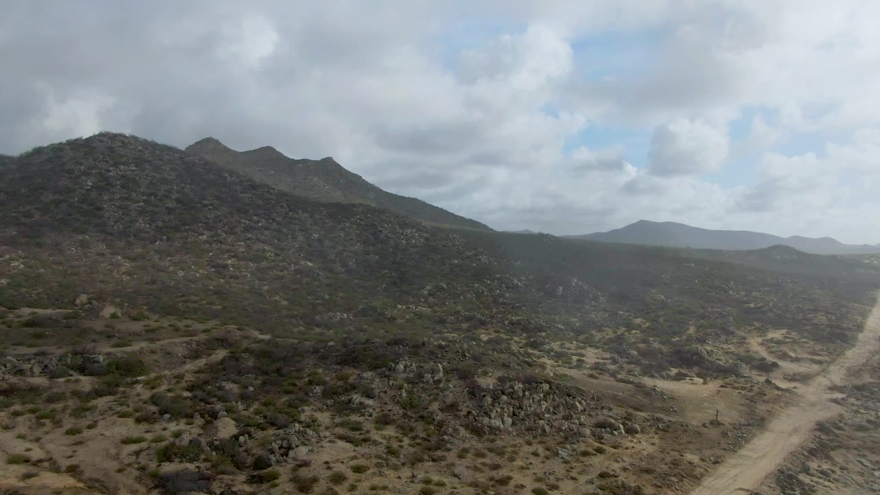 Aerial view in Punta Gorda, Baja California Sur, showing rocky hills, sparse scrub, a pale dirt road entering the valley, and no visible people.