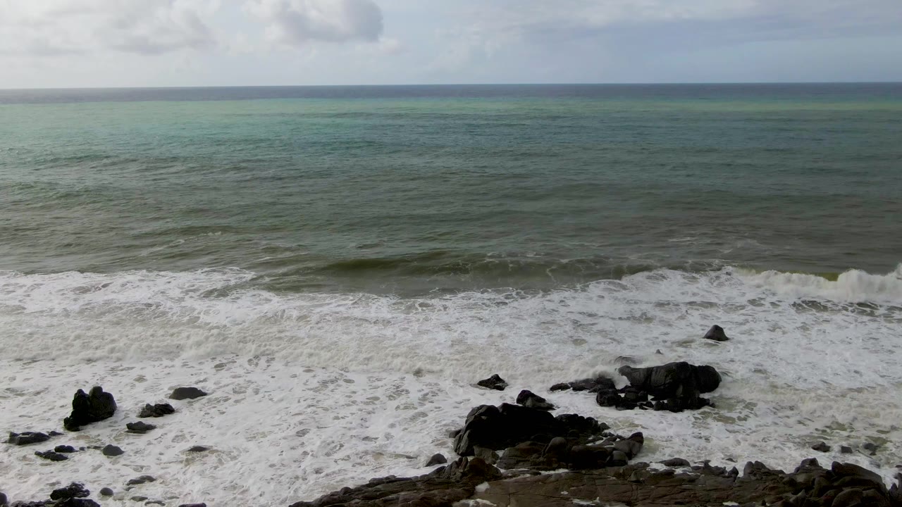 Foamy waves pushing around scattered black rocks near shore.