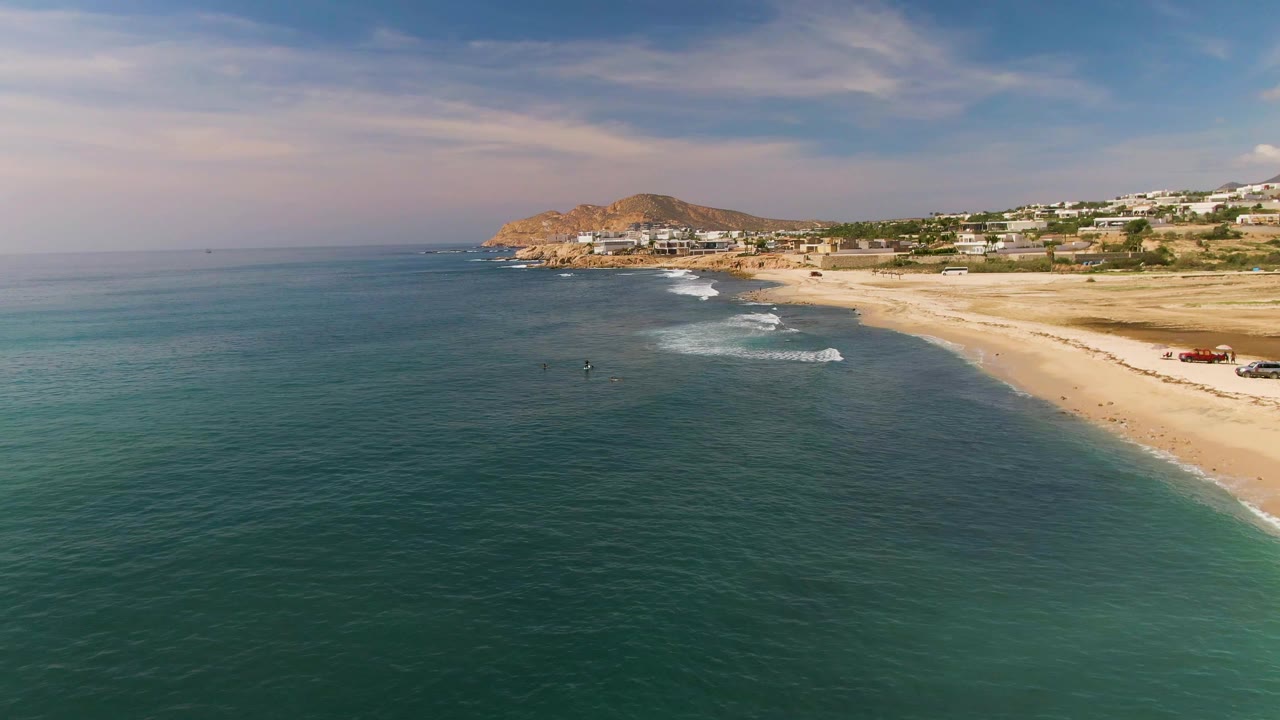 Aerial coastline view with ocean foreground and beach buildings in the distance.