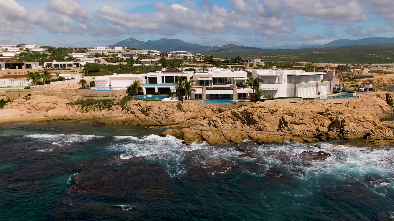Ocean waves breaking below white buildings on a rocky coast