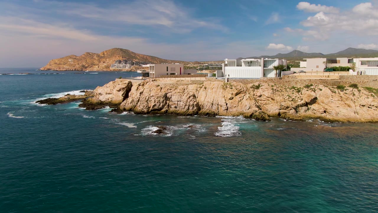 Wide ocean foreground with waves breaking against a rocky Los Cabos shore.