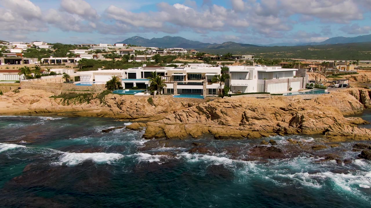 Wide aerial coastline with houses above rocks and waves