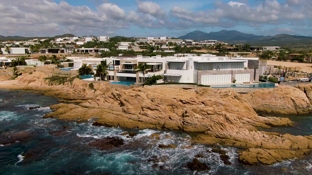 Waves wash over dark rocks below tan coastal bluff and homes