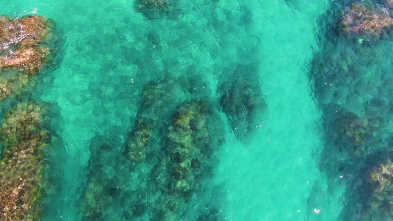 Shallow turquoise water with darker seabed patches and rocks.