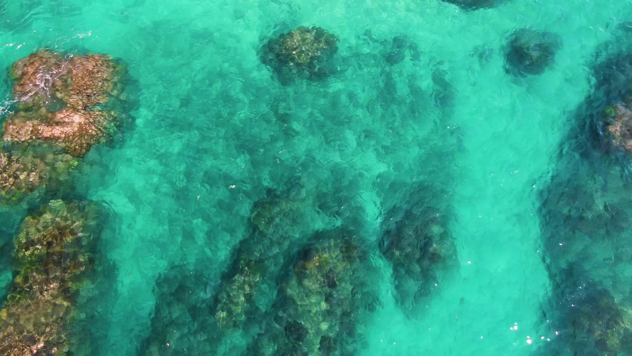 Turquoise shallow water over dark underwater rocks.