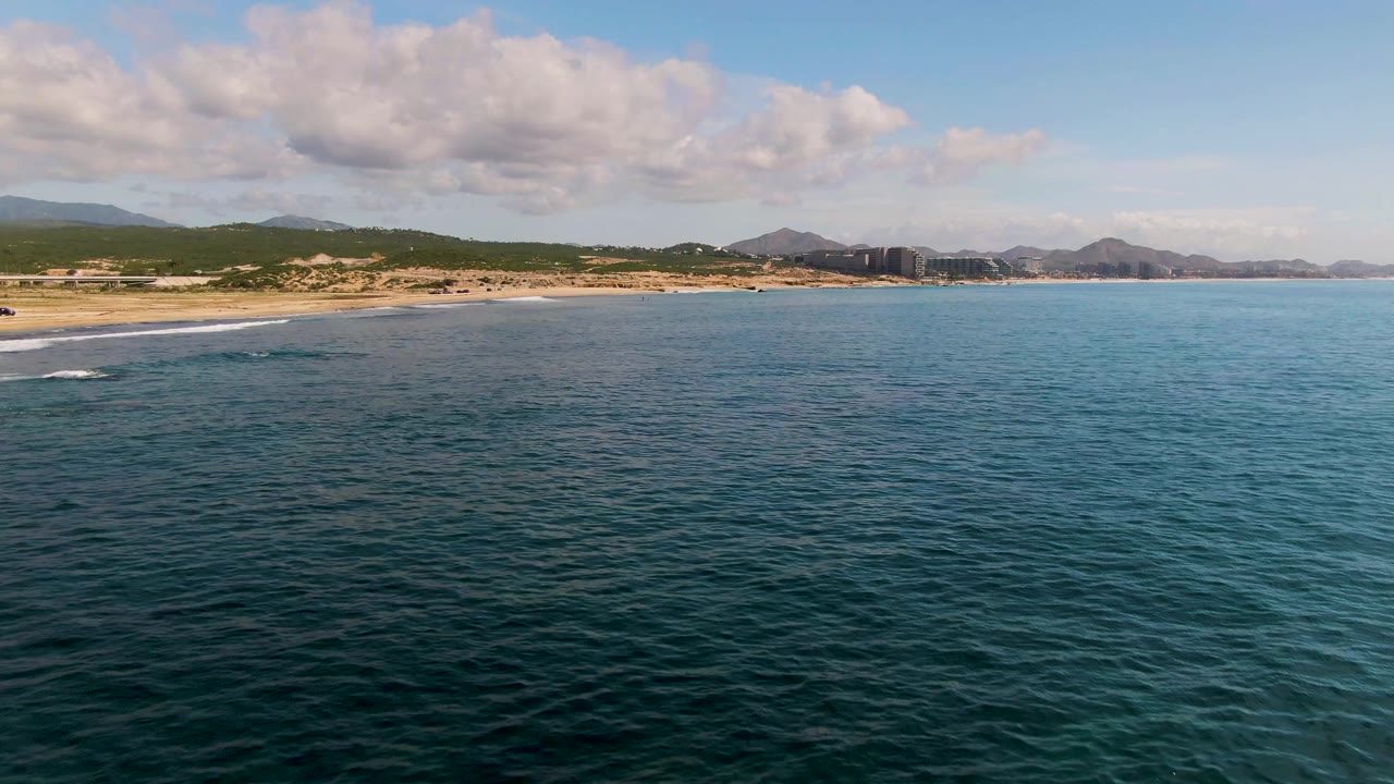 Blue ocean water with small waves near a sandy beach and mountain horizon.