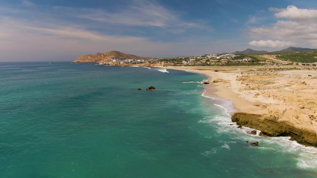 Aerial beach scene with waves breaking beside tan rocks and turquoise water.