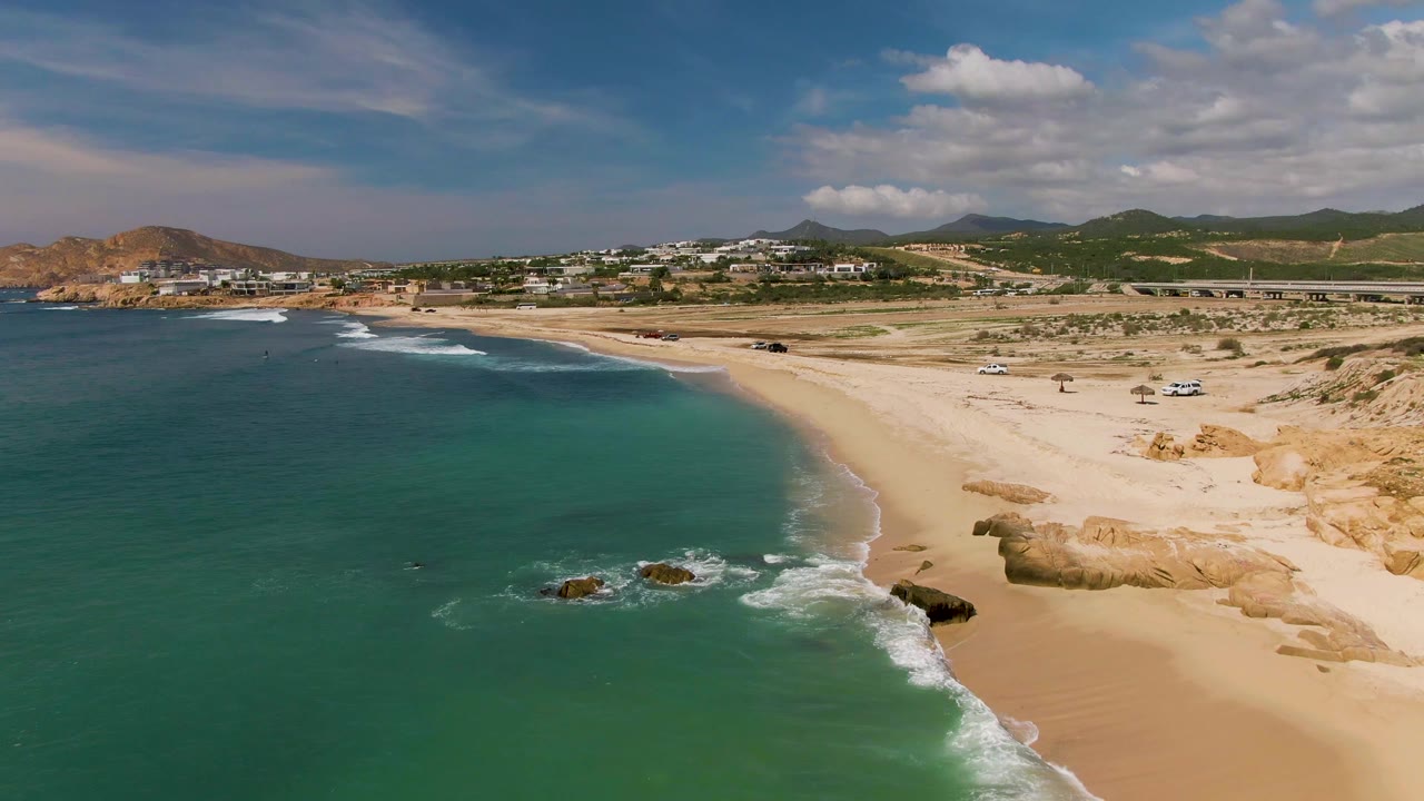 Turquoise waves reach a sandy shore with rocks and beach vehicles nearby.