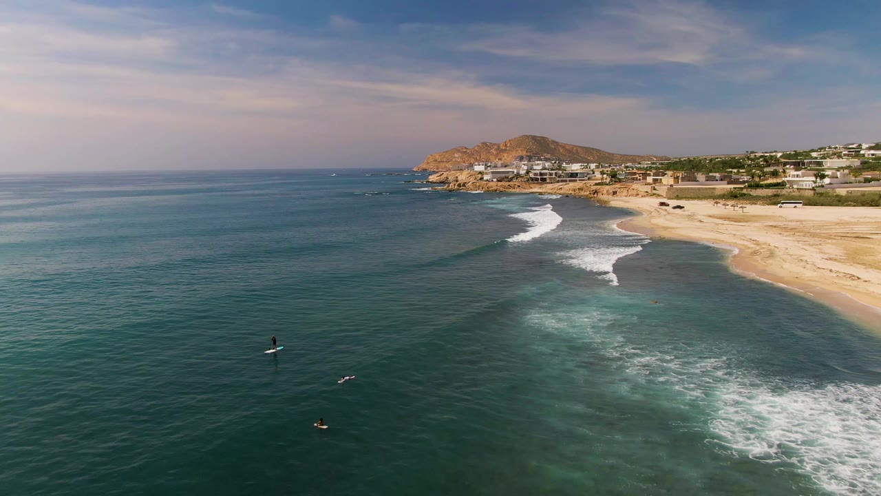 Board riders sit farther apart in the ocean as waves roll toward the beach.