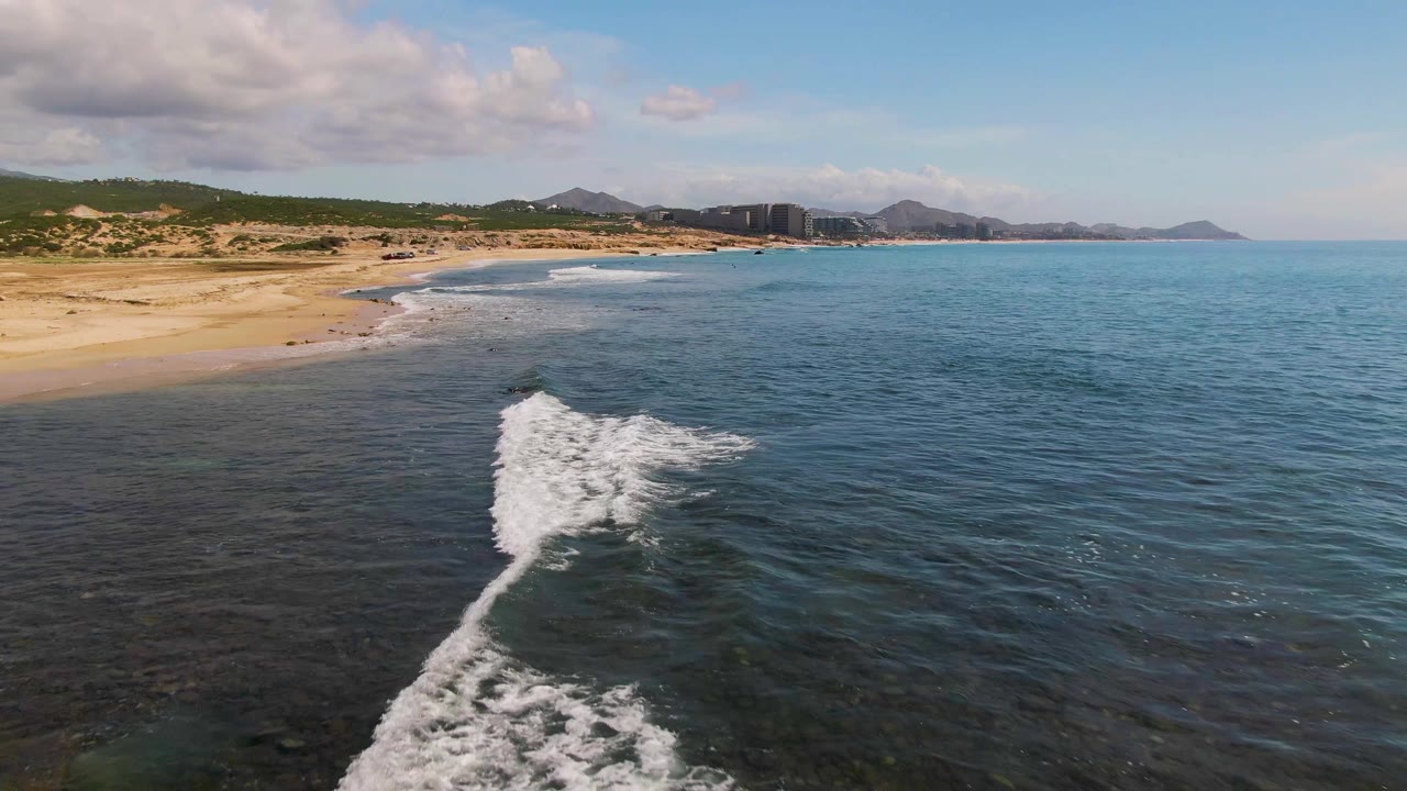 Foamy wave reaches the foreground near a broad sandy beach.