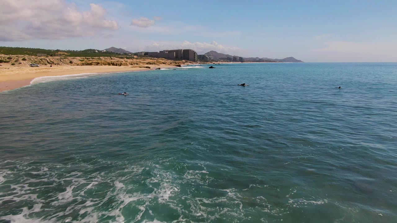 Swimmers float in calm ocean water beside a sandy shoreline.