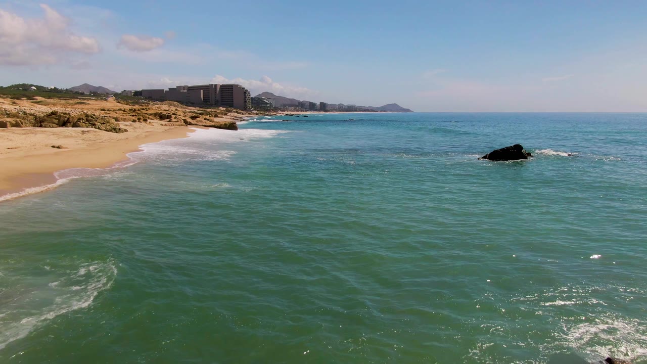 Sandy beach and green-blue ocean with a dark offshore rock