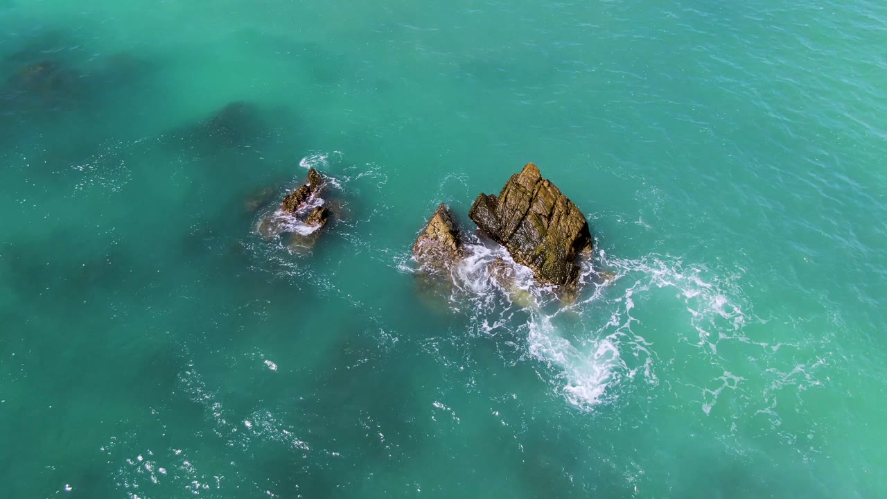 Overhead El Tule Los Cabos frame showing fresh whitewater breaking beside the larger exposed rock, a smaller rock nearby, and no visible people.