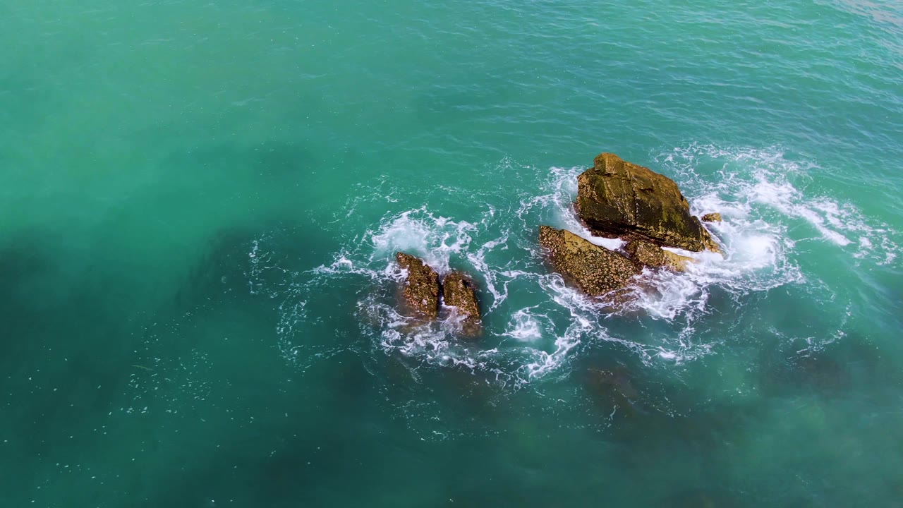 Aerial view of ocean foam curling around coastal rocks.