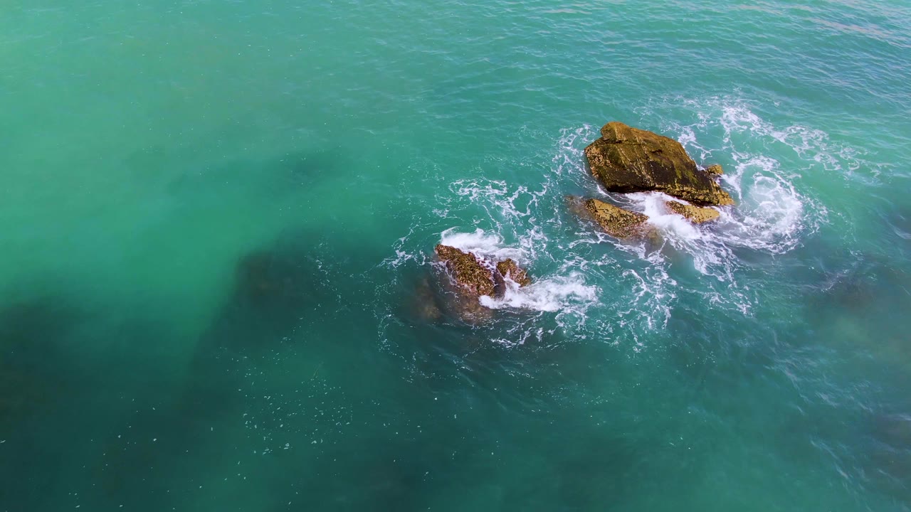 Overhead turquoise ocean with two rocky outcrops and white surf