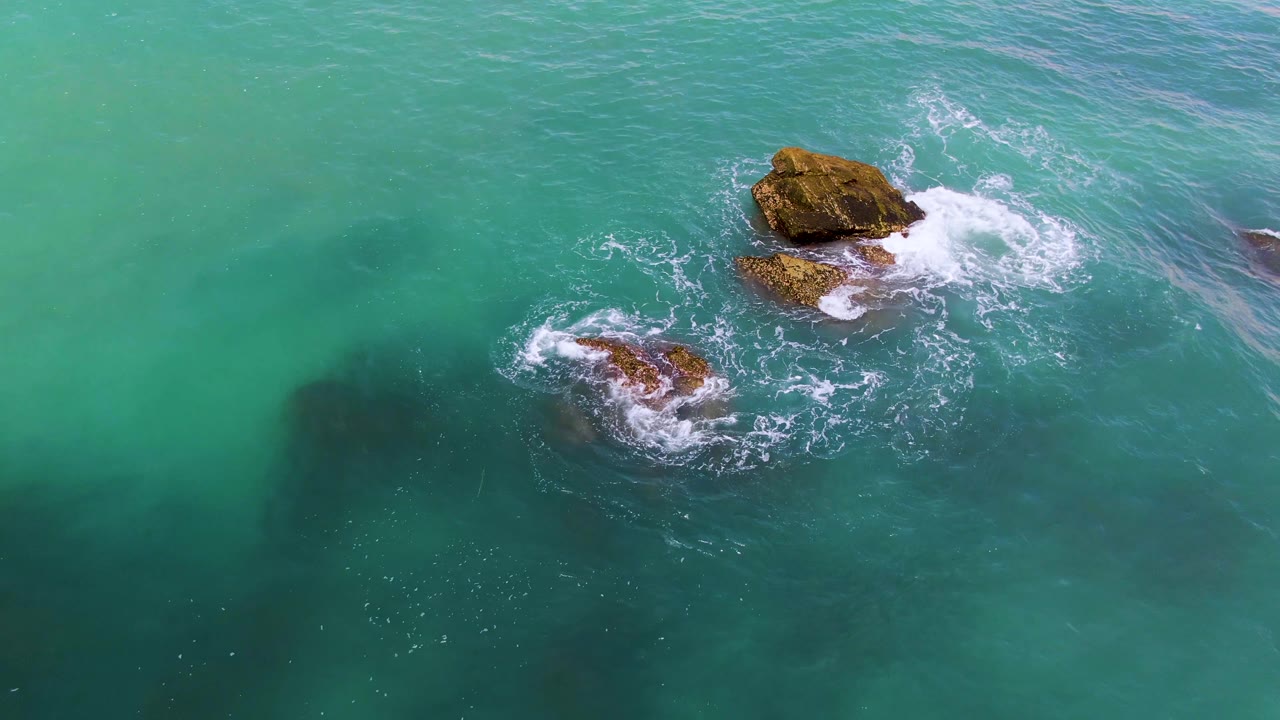 Overhead El Tule Los Cabos ocean view with two separated rocks, foamy surf rings around each outcrop, open turquoise water, and no visible people.