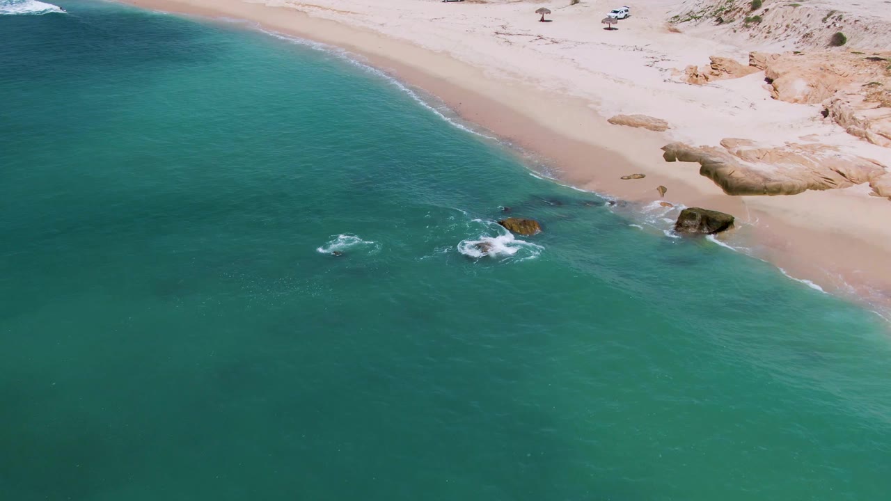 Turquoise water and sandy shoreline with white foam forming around rocks.