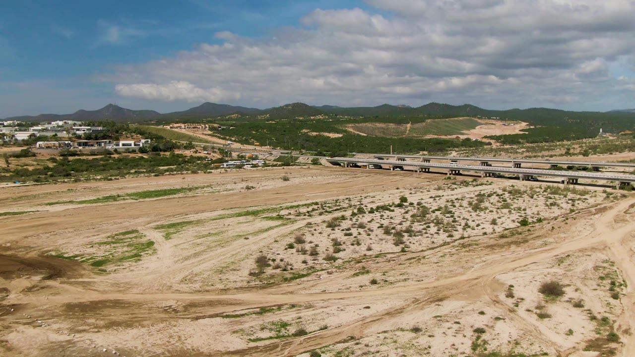 Dry riverbed foreground with bridge, hillside buildings, and mountains