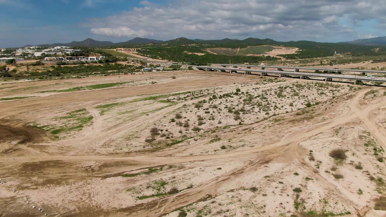 Vehicle on a bridge over an arid sandy wash with dirt tracks below.