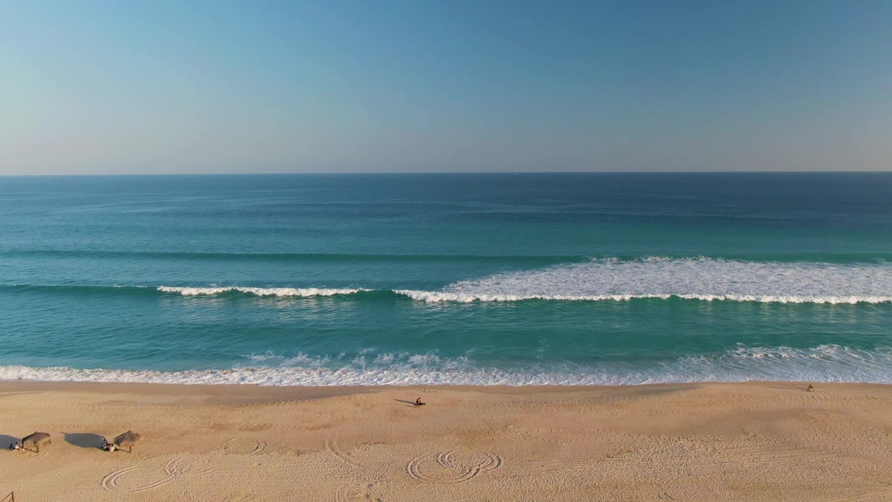 Wide aerial view of waves approaching a sandy beach.