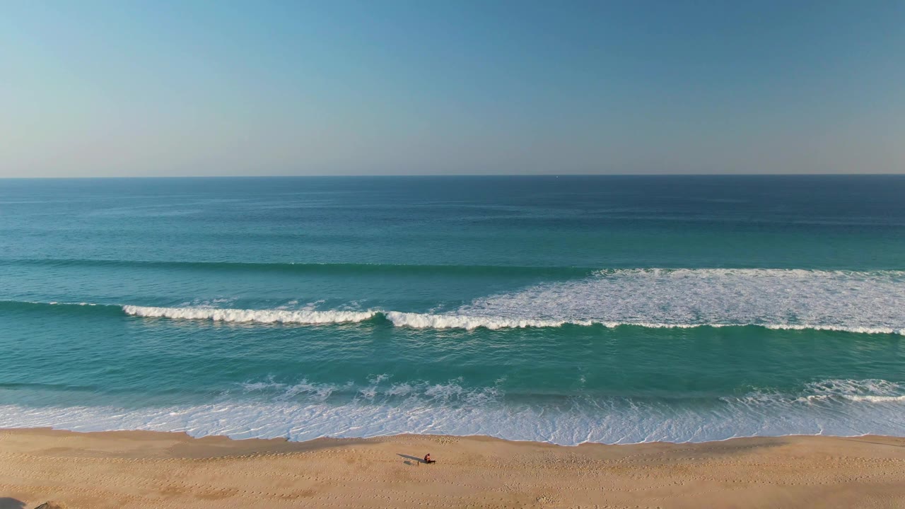 Aerial San Jose del Cabo beach frame with white foam spreading across the shoreline and open blue ocean beyond, with little beach area remaining at the bottom.