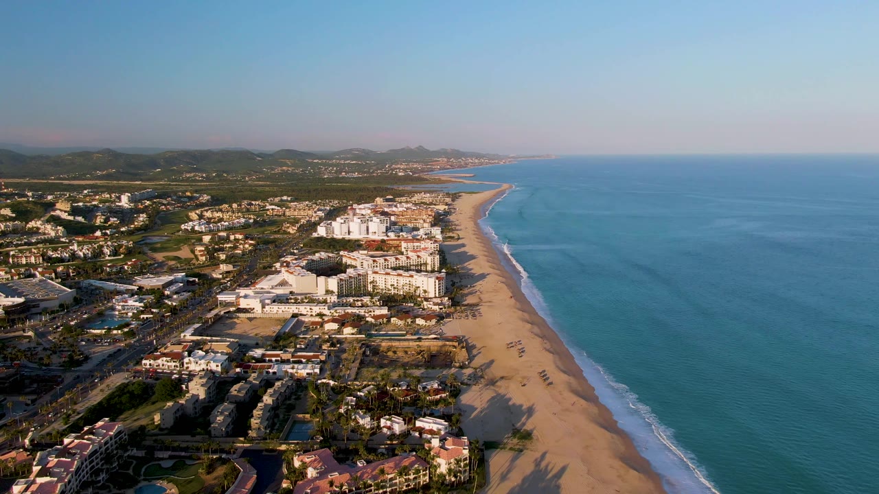 Aerial view down a long beach with ocean and town buildings.