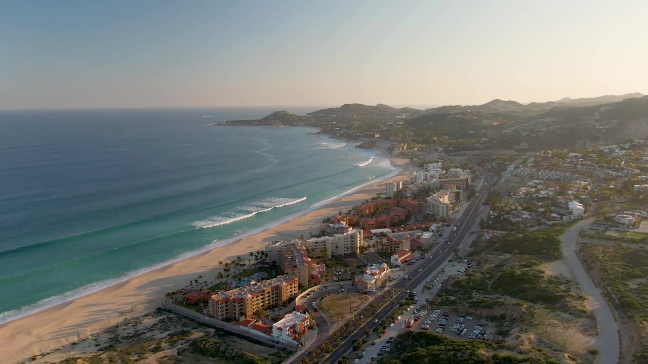 Ocean waves near a sandy beach with coastal buildings and hills beyond