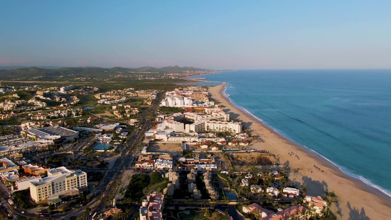 Coastal road traffic runs beside a sandy beach and blue ocean.