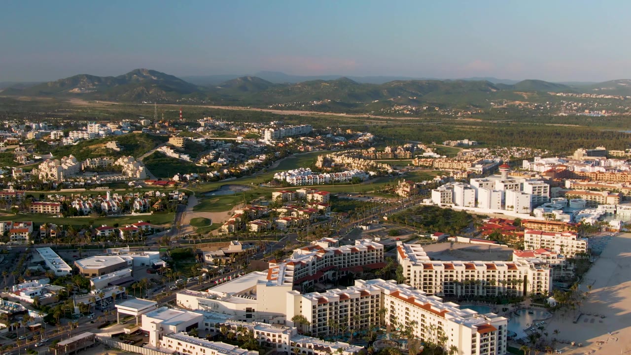 Elevated coastal city panorama with beach, buildings, roads, greenery, and hills.