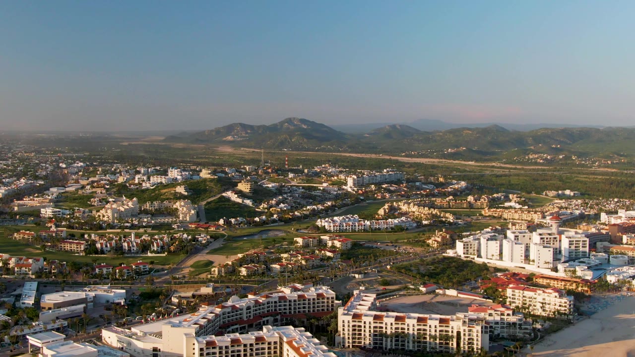 High aerial view of city blocks, resort-style buildings, beach, and mountains
