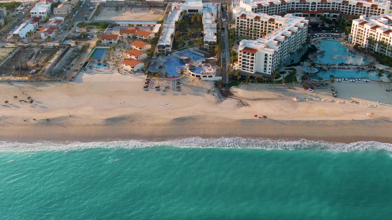 Aerial view of beachfront hotels, pools, sand, and turquoise ocean.